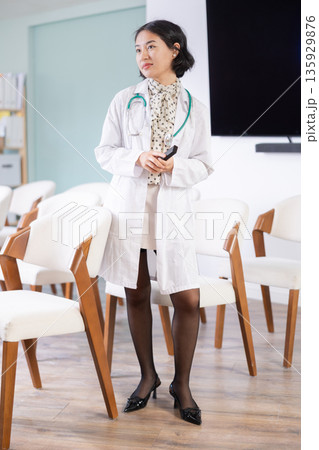 Young woman in medical coat giving lecture with remote control 135929876
