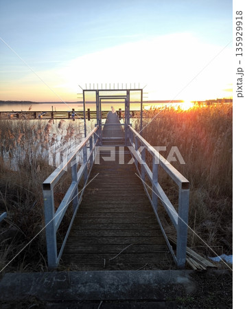 A wooden pier with metal gates against the backdrop of a bright sunset over the lake A wooden pier with metal gates against the backdrop of a bright sunset over the lake 135929918