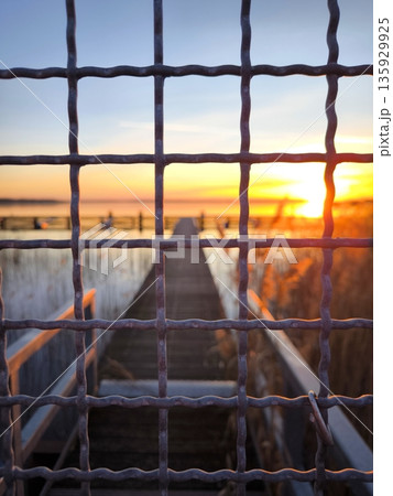 Beautiful sunset over the lake and pier through the metal mesh fence Beautiful sunset over the lake and pier through the metal mesh fence 135929925