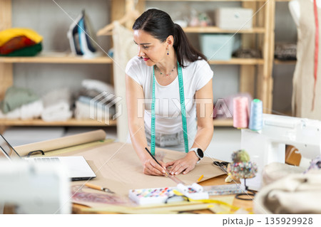Woman dressmaker draws pattern using drawing on laptop 135929928