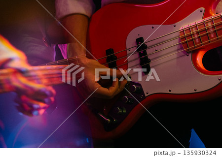 Close-up of hands playing red electric bass guitar on stage Close-up of hands playing red electric bass guitar on stage 135930324