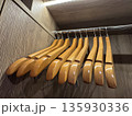 Wooden clothes hangers hanging on a metal rod inside a wooden wardrobe, with an LED light strip above. 135930336