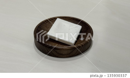 White bar soap on wooden soap dish on white surface, close-up White bar soap on wooden soap dish on white surface, close-up 135930337