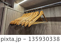 Wooden clothes hangers hanging on a metal rod inside a wooden wardrobe, with an LED light strip above. 135930338