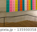 London, UK, October 22, 2019 Interior stairway with wooden steps, concrete wall, black handrail and a large multicolor poster of text blocks mounted above the stairs. 135930358