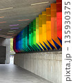 Concrete underpass with hanging rainbow panels along the wall, colored LED strip lights on the ceiling, and walkway leading outside. 135930375