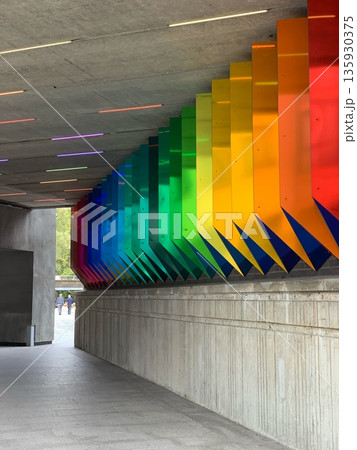 Concrete underpass with hanging rainbow panels along the wall, colored LED strip lights on the ceiling, and walkway leading outside. Concrete underpass with hanging rainbow panels along the wall, colored LED strip lights on the ceiling, and walkway leading outside. 135930375
