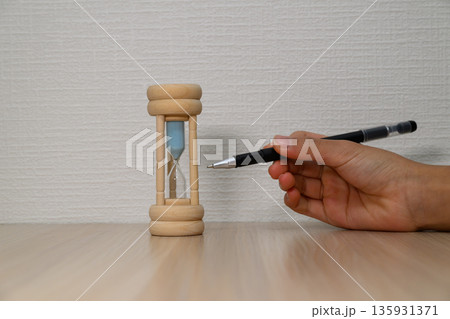 砂時計をペンで指す手とコピースペース 135931371