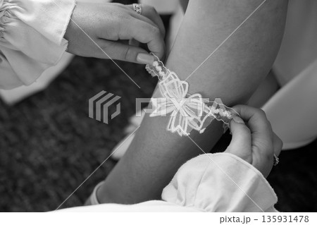 Black and White Close-Up of Bride Wearing Lace Garter Being Adjusted by Hand During Wedding Preparation 135931478
