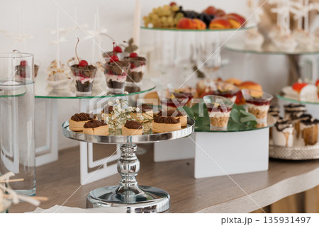 Elegant Dessert Buffet Display with Chocolate Tarts, Fruit Arrangements, and Glass Tiered Stands in Soft White and Gold Lighting 135931497