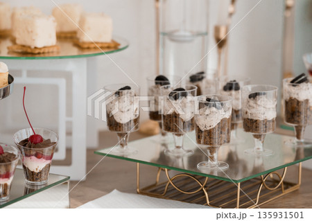 Elegant Dessert Buffet Display Featuring Mini Oreo Cheesecakes in Glass Cups and Creamy White Pastries on Tiered Stands 135931501