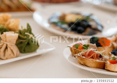 Elegant Appetizer Platter with Crostini, Prosciutto, Olives, and Fresh Herbs on White Tablecloth 135931512