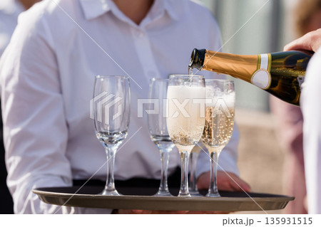 Waiter Pouring Champagne into Flutes at Luxury Event with White Shirt and Gold Bottle Waiter Pouring Champagne into Flutes at Luxury Event with White Shirt and Gold Bottle 135931515