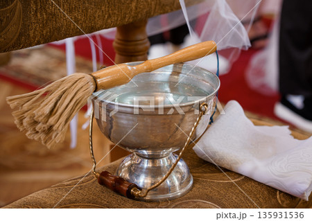 Silver Baptismal Basin with Wooden Dipper and White Cloth on Ornate Fabric Surface Silver Baptismal Basin with Wooden Dipper and White Cloth on Ornate Fabric Surface 135931536