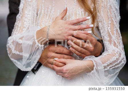 Close-up of bride and groom's hands with wedding rings, white lace dress, soft natural lighting, romantic intimate moment Close-up of bride and groom's hands with wedding rings, white lace dress, soft natural lighting, romantic intimate moment 135931550