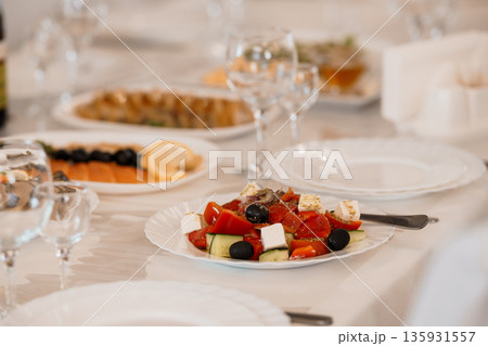Elegant Greek Salad with Fresh Tomatoes Cucumbers Feta Cheese and Olives Served on White Plate at Fine Dining Table Elegant Greek Salad with Fresh Tomatoes Cucumbers Feta Cheese and Olives Served on White Plate at Fine Dining Table 135931557