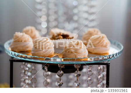Elegant White Meringue Desserts on Crystal Tray with Sparkling Chandelier Background Elegant White Meringue Desserts on Crystal Tray with Sparkling Chandelier Background 135931561