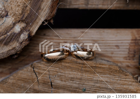 Elegant Gold Wedding Rings with Diamond Engagement Ring Resting on Rustic Wooden Surface 135931585