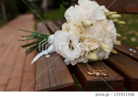 White Wedding Bouquet with Gold Rings on Wooden Bench in Garden Setting White Wedding Bouquet with Gold Rings on Wooden Bench in Garden Setting 135931586