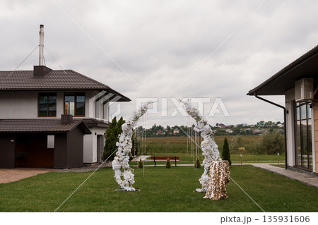 Elegant White Floral Wedding Arch?? in Outdoor Garden Setting with Modern House Background 135931606