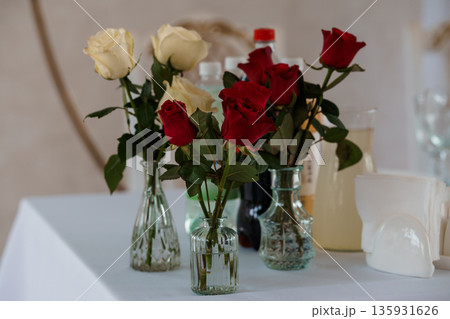 Elegant Red and White Rose Bouquet in Glass Vases on a Table with Beverage Bottles and Napkins 135931626