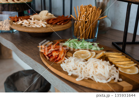 Assorted Snacks and Beverages Displayed on Wooden Table with Pretzels, Lemon Slices, and Shredded Ingredients in Natural Lighting 135931644