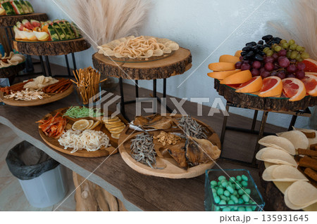 Rustic Wooden Buffet Table with Assorted Snacks, Fresh Fruits, and Seafood Display in Warm Natural Lighting 135931645