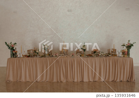 Elegant Long Banquet Table with Gold Candles and Floral Arrangements in Soft Beige Linen Setting Elegant Long Banquet Table with Gold Candles and Floral Arrangements in Soft Beige Linen Setting 135931646