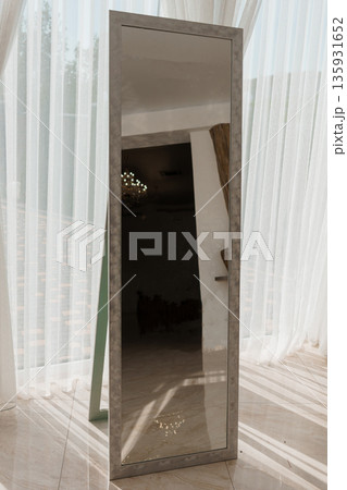 Full-Length Floor Mirror with Textured Frame in Sunlit Room with Sheer Curtains and Marble Flooring Full-Length Floor Mirror with Textured Frame in Sunlit Room with Sheer Curtains and Marble Flooring 135931652