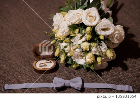 Elegant White Rose Wedding Bouquet with Gold Rings in Wooden Box and Gray Bow Tie on Brown Fabric Background Elegant White Rose Wedding Bouquet with Gold Rings in Wooden Box and Gray Bow Tie on Brown Fabric Background 135931654