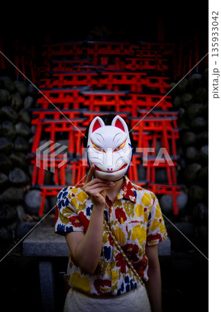 神社の境内で狐のお面をつけた女性のポートレート 135933042