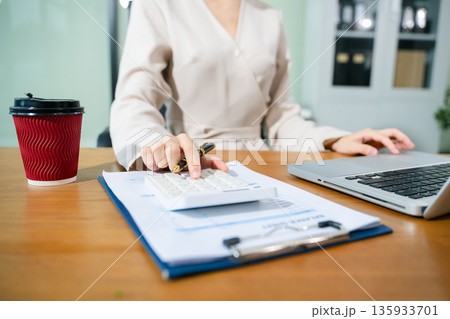 Women counting coins on calculator taking from the piggy bank. hand holding pen working on calculator to calculate on desk 135933701