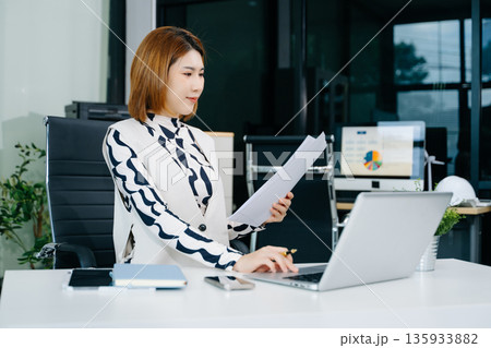 Young beautiful woman typing on tablet and laptop while sitting at the working white table in office Young beautiful woman typing on tablet and laptop while sitting at the working white table in office 135933882