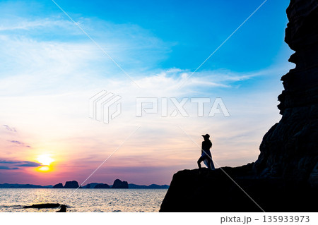 Beautiful young woman silhouette standing on stone at sunset or sunrise sky over sea Beautiful young woman silhouette standing on stone at sunset or sunrise sky over sea 135933973