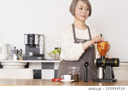 キッチンでコーヒーミルでコーヒー豆を挽きエスプレッソマシーンでエスプレッソを入れるシニア女性 キッチンでコーヒーミルでコーヒー豆を挽きエスプレッソマシーンでエスプレッソを入れるシニア女性 135934514
