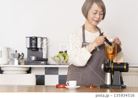 キッチンでコーヒーミルでコーヒー豆を挽きエスプレッソマシーンでエスプレッソを入れるシニア女性 キッチンでコーヒーミルでコーヒー豆を挽きエスプレッソマシーンでエスプレッソを入れるシニア女性 135934516