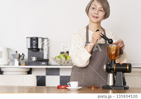 キッチンでコーヒーミルでコーヒー豆を挽きエスプレッソマシーンでエスプレッソを入れるシニア女性 135934520