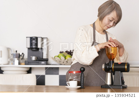 キッチンでコーヒーミルでコーヒー豆を挽きエスプレッソマシーンでエスプレッソを入れるシニア女性 135934521