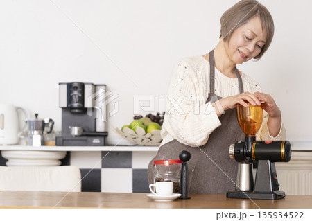 キッチンでコーヒーミルでコーヒー豆を挽きエスプレッソマシーンでエスプレッソを入れるシニア女性 135934522