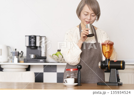 キッチンでコーヒーミルでコーヒー豆を挽きエスプレッソマシーンでエスプレッソを入れるシニア女性 キッチンでコーヒーミルでコーヒー豆を挽きエスプレッソマシーンでエスプレッソを入れるシニア女性 135934524