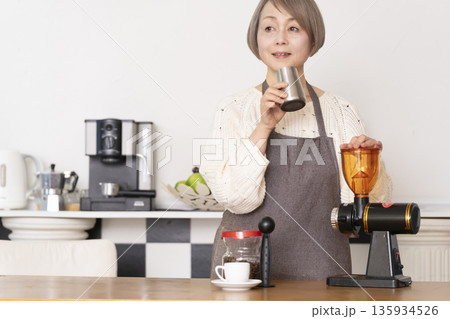 キッチンでコーヒーミルでコーヒー豆を挽きエスプレッソマシーンでエスプレッソを入れるシニア女性 135934526