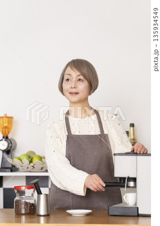 キッチンでコーヒーミルでコーヒー豆を挽きエスプレッソマシーンでエスプレッソを入れるシニア女性 キッチンでコーヒーミルでコーヒー豆を挽きエスプレッソマシーンでエスプレッソを入れるシニア女性 135934549