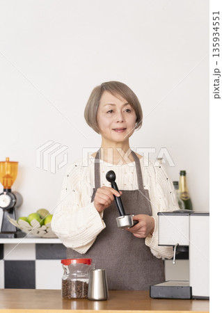 キッチンでコーヒーミルでコーヒー豆を挽きエスプレッソマシーンでエスプレッソを入れるシニア女性 135934551