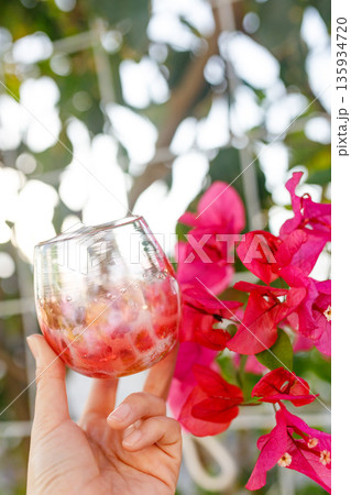 ブーゲンビリアの花と手に持つ琉球ガラスのグラス 135934720