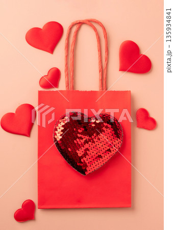 Red gift bag with sequin heart and decorative hearts on pastel background 135934841
