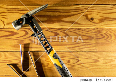 A high quality premium claw hammer accompanied by assorted nails, placed on a rustic wooden table surface, copy space, top view 135935961