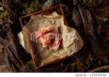 Prosciutto with rosemary on a paper in wooden box. Prosciutto with rosemary on a paper in wooden box. 135936186