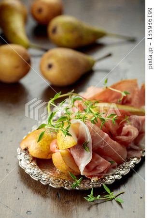 Prosciutto with pears and thyme on a silver tray. 135936199