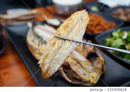 Chopsticks lifting a piece of crispy, golden grilled mackerel fillet at a Korean restaurant Chopsticks lifting a piece of crispy, golden grilled mackerel fillet at a Korean restaurant 135936628