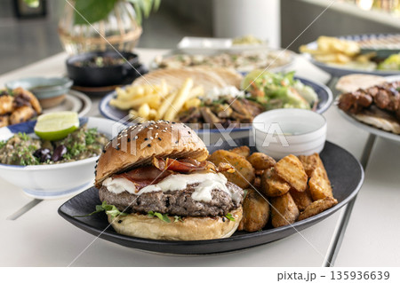 Gourmet wagyu beef burger wirh bacon, cheese and wedge fries on outdoor white cafe table Gourmet wagyu beef burger wirh bacon, cheese and wedge fries on outdoor white cafe table 135936639